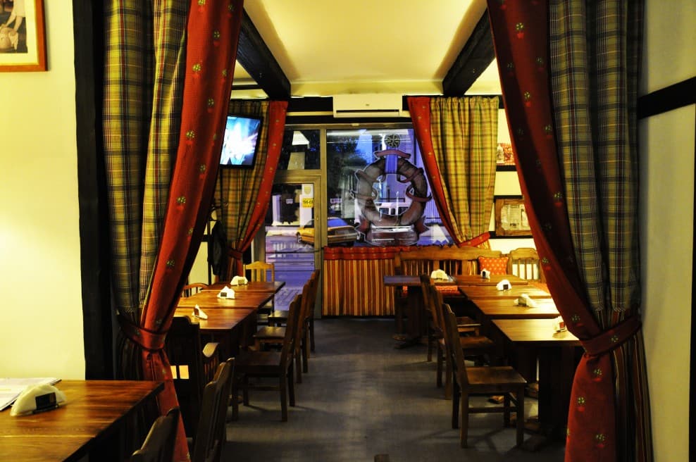 Sala restauracyjna z drewnianymi stołami i czerwonymi zasłonami